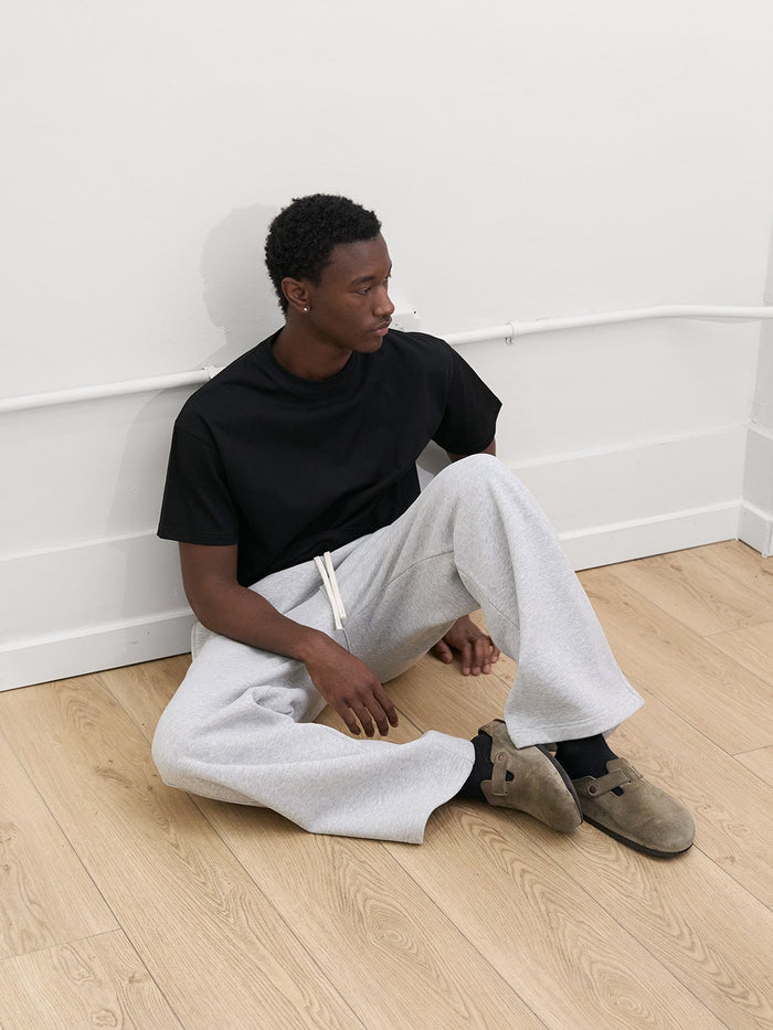 male model sitting wearing black tshirt and heather gray sweatpants by one dna