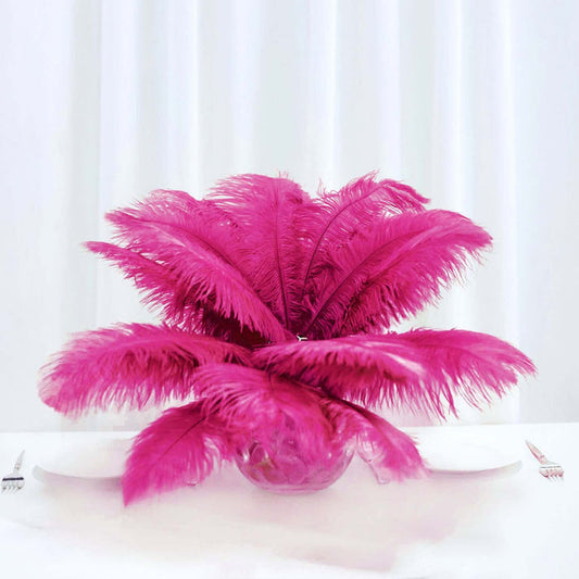 Pink feather centerpiece in glass vase on white table.