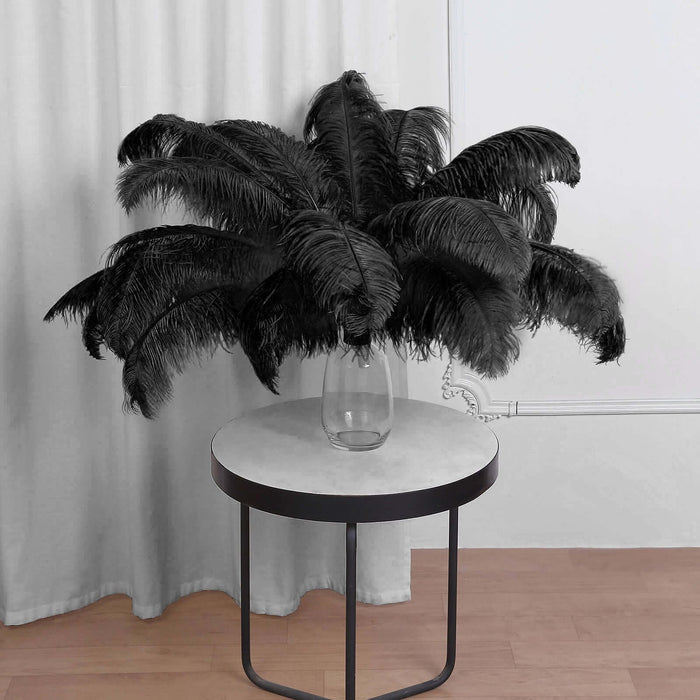 Black feather arrangement in a glass vase on a round table.
