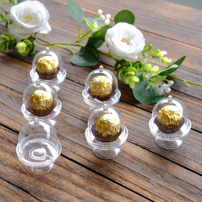 Chocolate truffles in clear dome displays with floral accents on wooden surface.