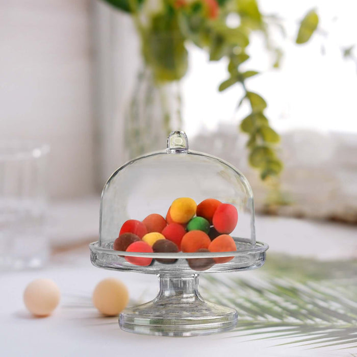 Glass dessert dome with colorful candies inside on a decorative stand.