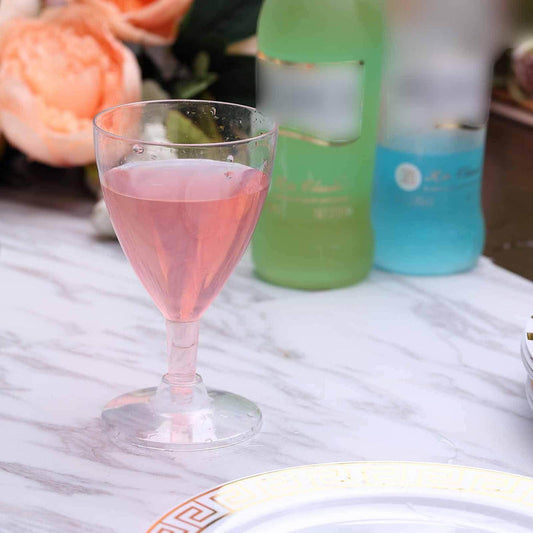 Pink drink in a clear glass on a marble table with blurred bottles in the background.