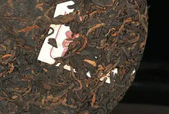 Compressed Chinese puerh tea cake with dark tea leaves and embedded paper ticket