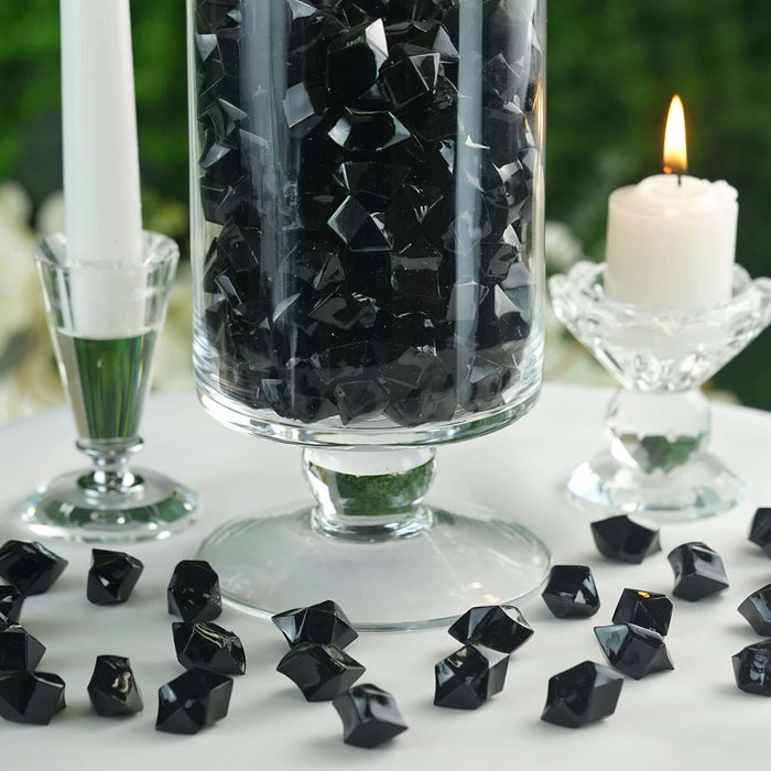Black decorative crystals in a glass vase with candles on a table.