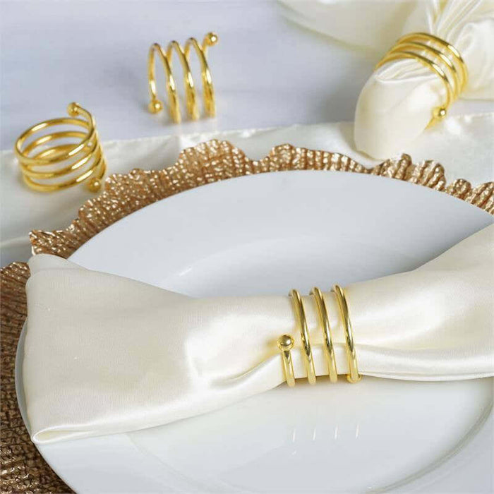 Gold napkin rings arranged on a white plate with a satin napkin.
