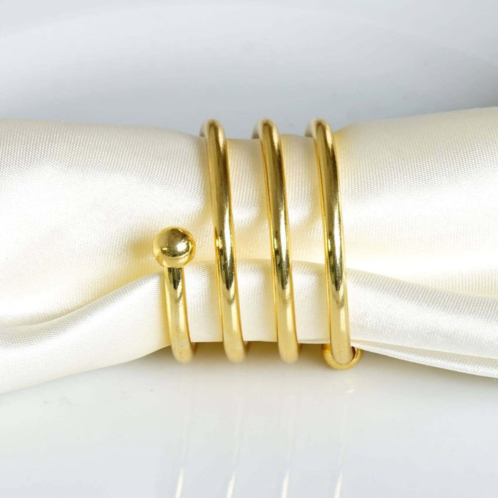 Gold napkin rings stacked on a satin napkin. #whtbkgd