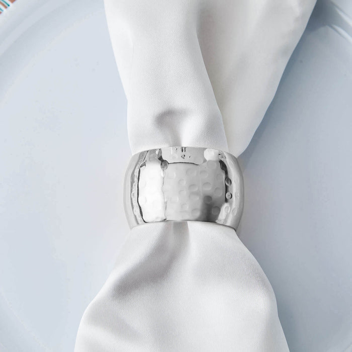 Silver napkin ring on a white napkin atop a plate.