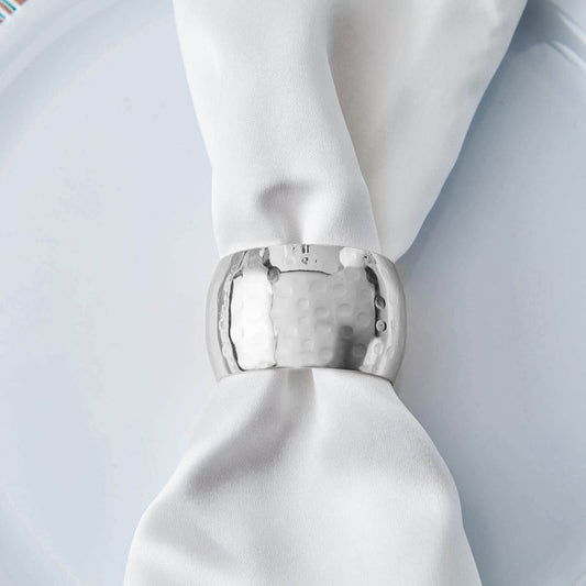 Silver napkin ring on a white napkin atop a plate.