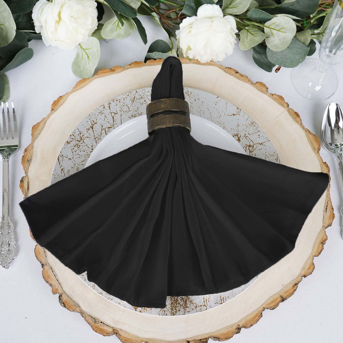Black pleated napkin with a decorative ring on a rustic wooden plate.