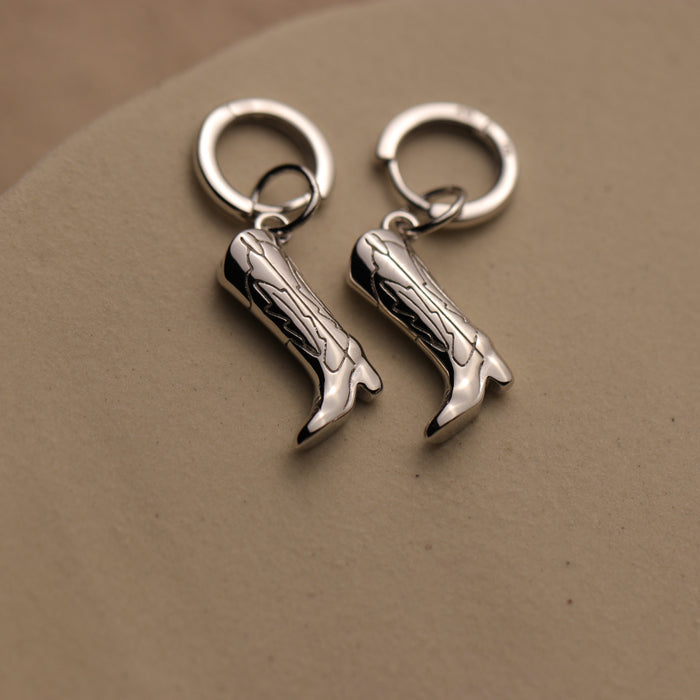 Silver cowboy boot earrings on a beige background