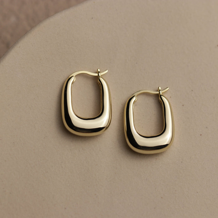 Gold hoop earrings shaped like a domed rectangle on a beige background