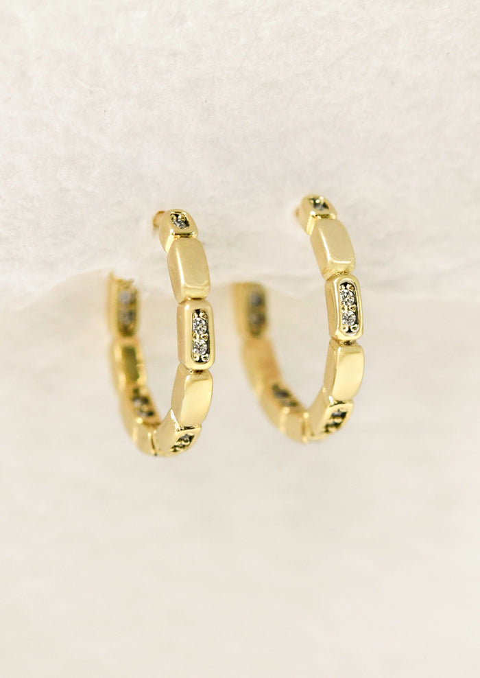 A pair of gold huggie hoop earrings with glass crystals.