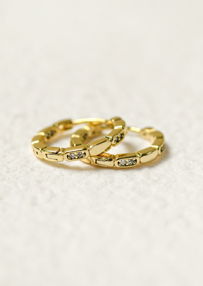 A pair of gold huggie hoop earrings with glass crystals.