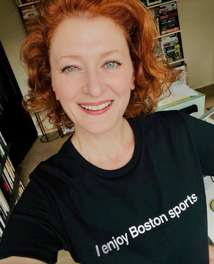 photo of a woman wearing black unisex t-shirt with the words i enjoy boston sports in white text