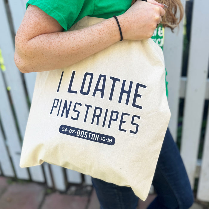 woman holding tan canvas tote bag with the red sox phrase i loathe pinstripes by the red seat
