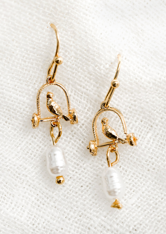 A pair of gold earrings depicting bird sitting on perch, with pearl bead.