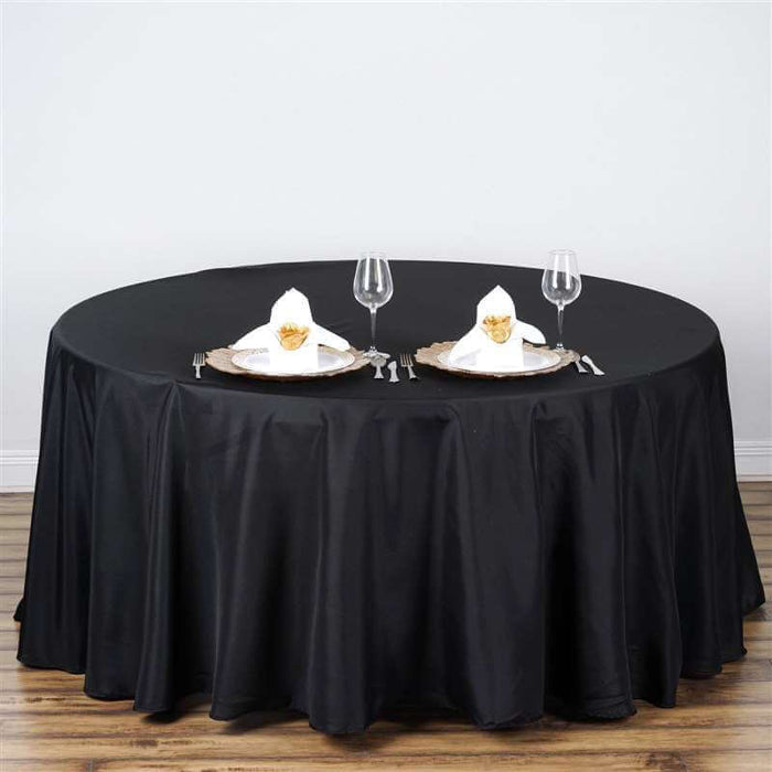 Round black tablecloth draped over a table set for two with elegant place settings.