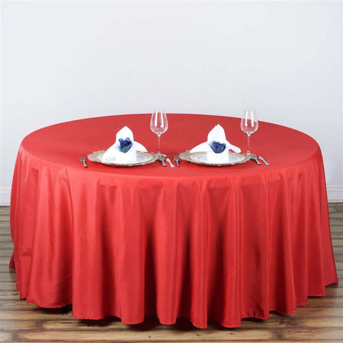 Red round tablecloth set for dining with plates and glasses.
