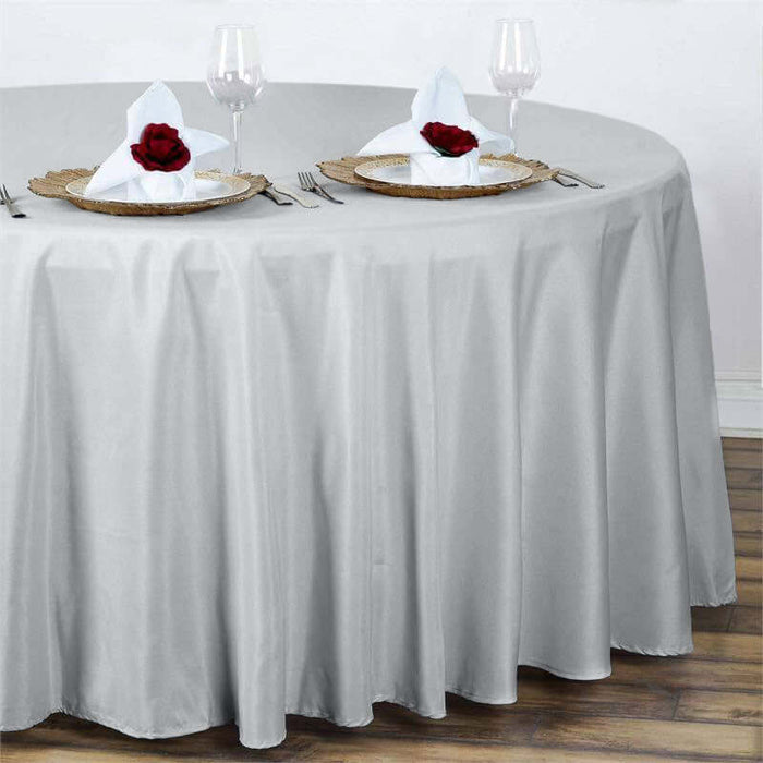 Elegant round silver tablecloth draped over a dining table with rose-adorned plates.
