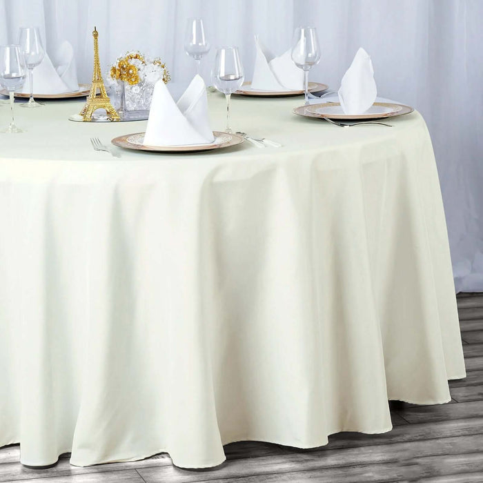 Elegant round table with a cream tablecloth set for dining, featuring glassware and decor.