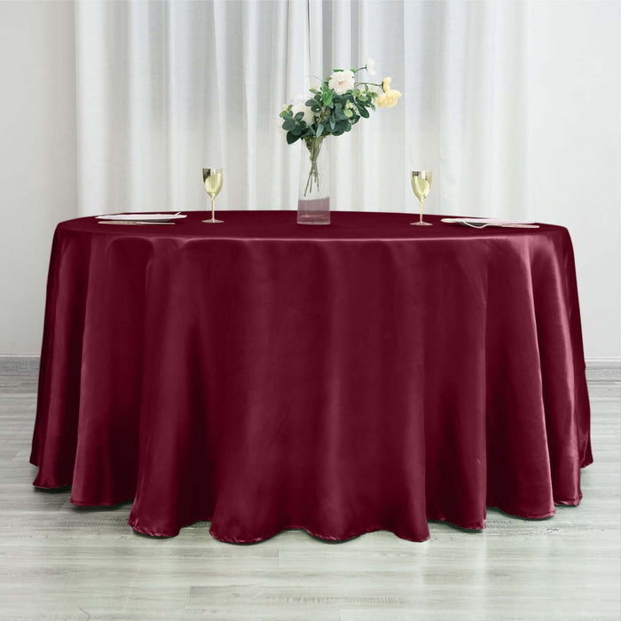 Burgundy tablecloth draped over a round table with floral centerpiece and glasses.