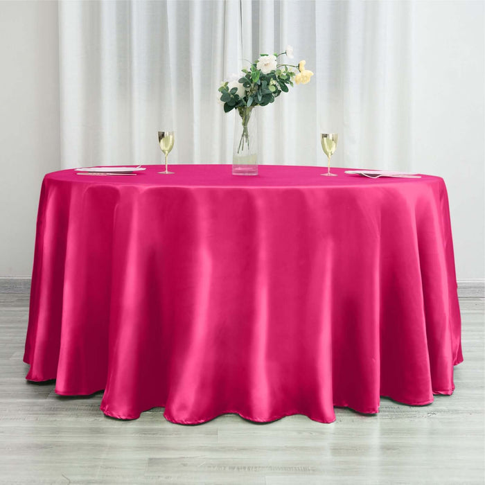 Pink tablecloth draped over a round table with decorative flowers and glassware.