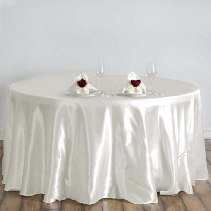 Elegant round table with a satin ivory tablecloth, set for dinner.