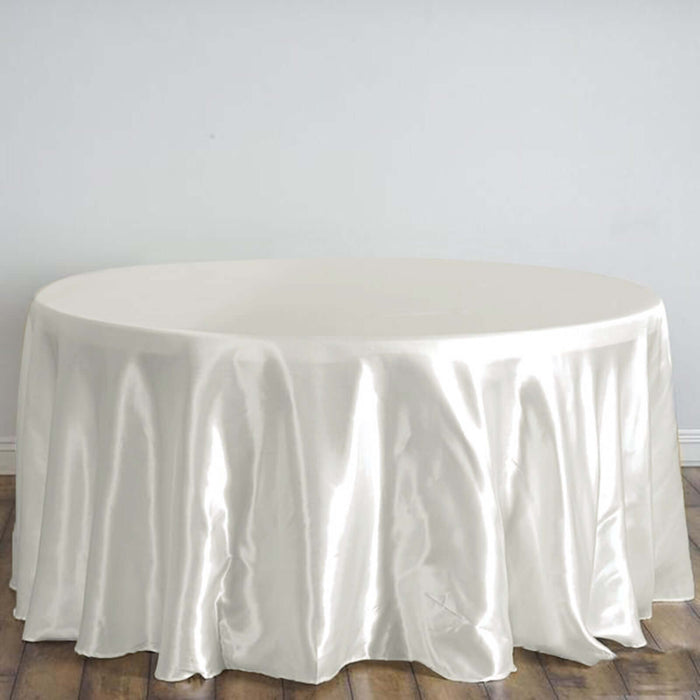 Round satin tablecloth in cream color on a wooden floor.