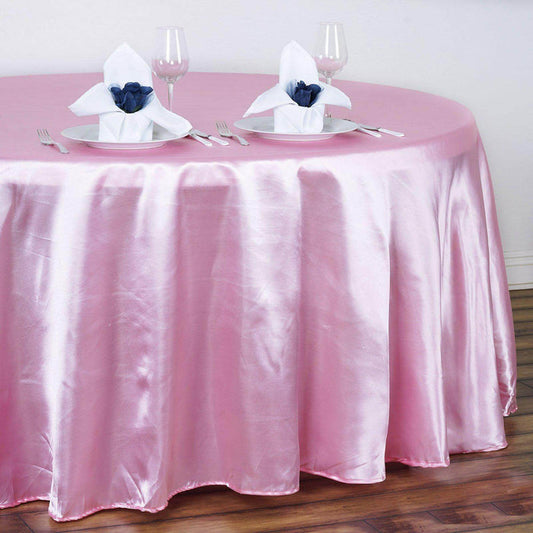 Pink satin tablecloth draped over a round table set with elegant napkins and glassware.