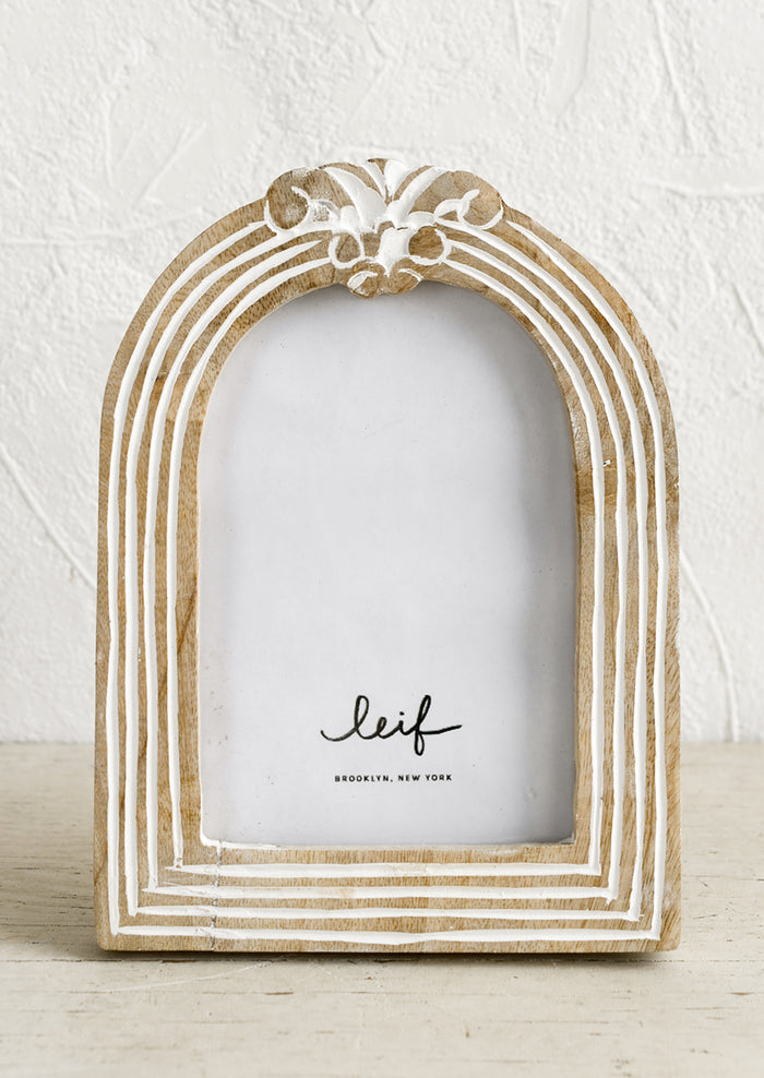 An arch shaped wooden picture frame with white paint detailing.