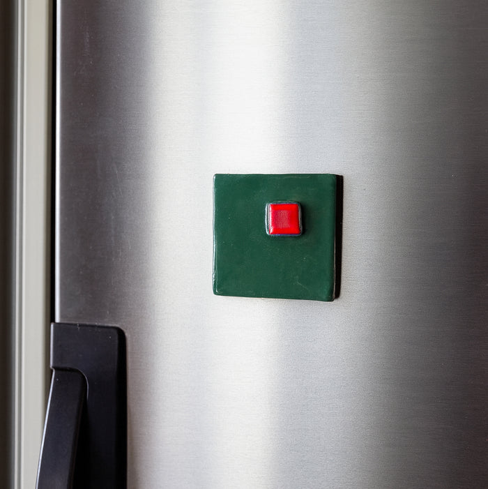 Green square magnet with a red button on a metallic surface