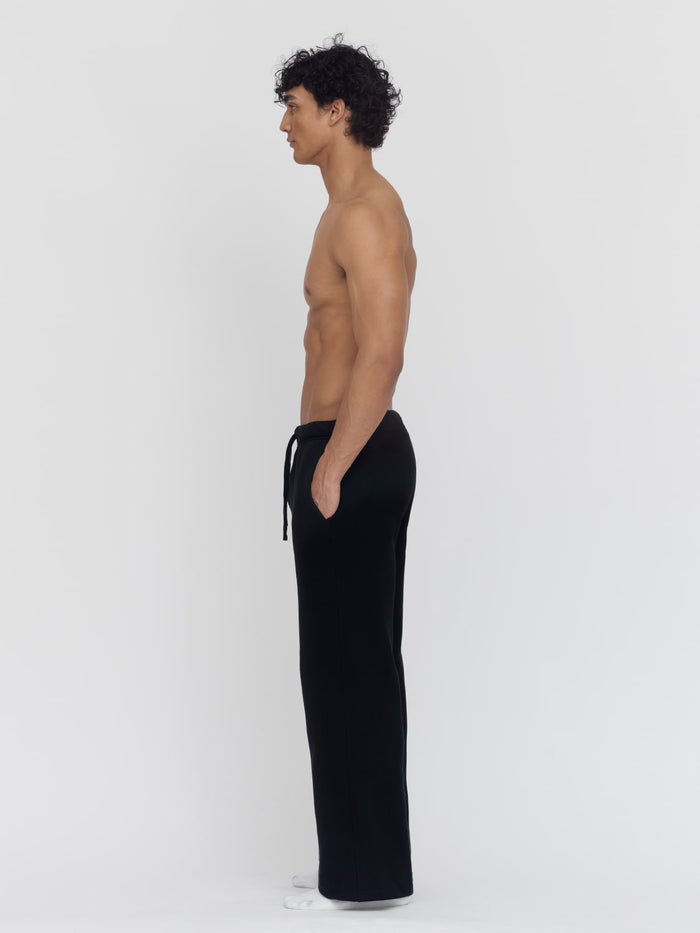 A male model, in profile, wears black wide-leg sweatpants by One Dna brand